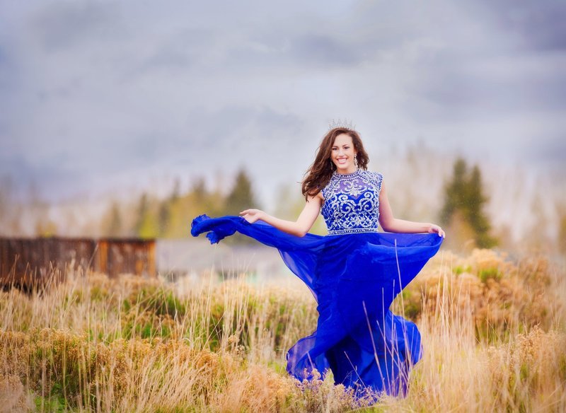 Senior girl dancing in the rain with a royal blue dress twirling in the rain by the Laramie river.