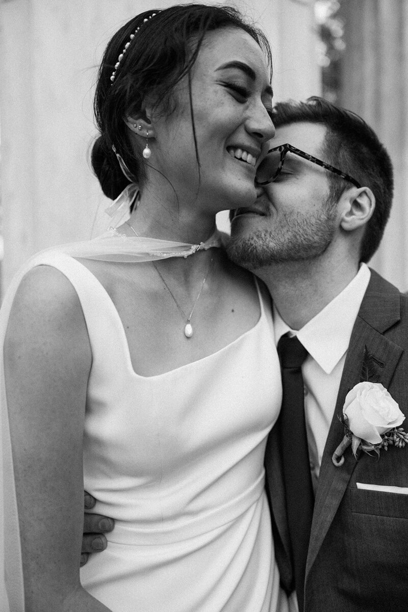 Black and white elegant profile shot of bride getting kissed by her groom
