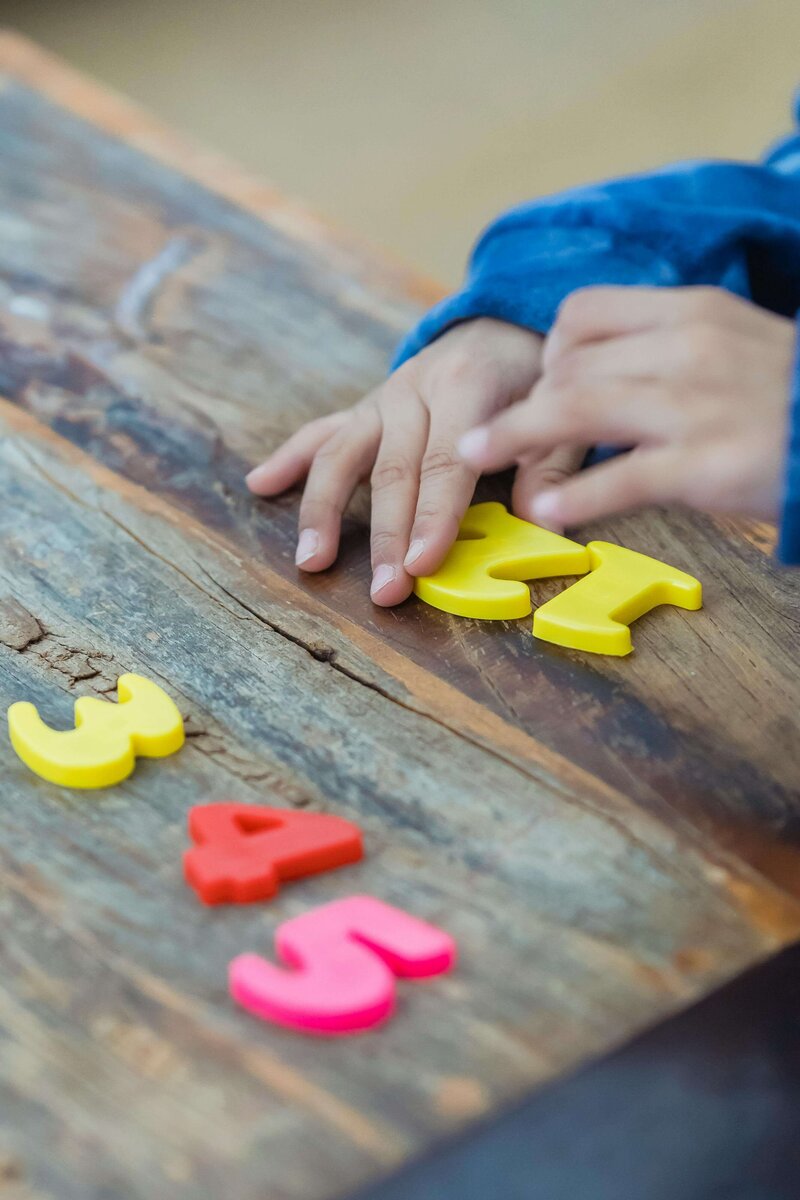 A child is playing with colorful plastic numbers on a wooden surface, arranging them in order while focusing on a yellow number "4."