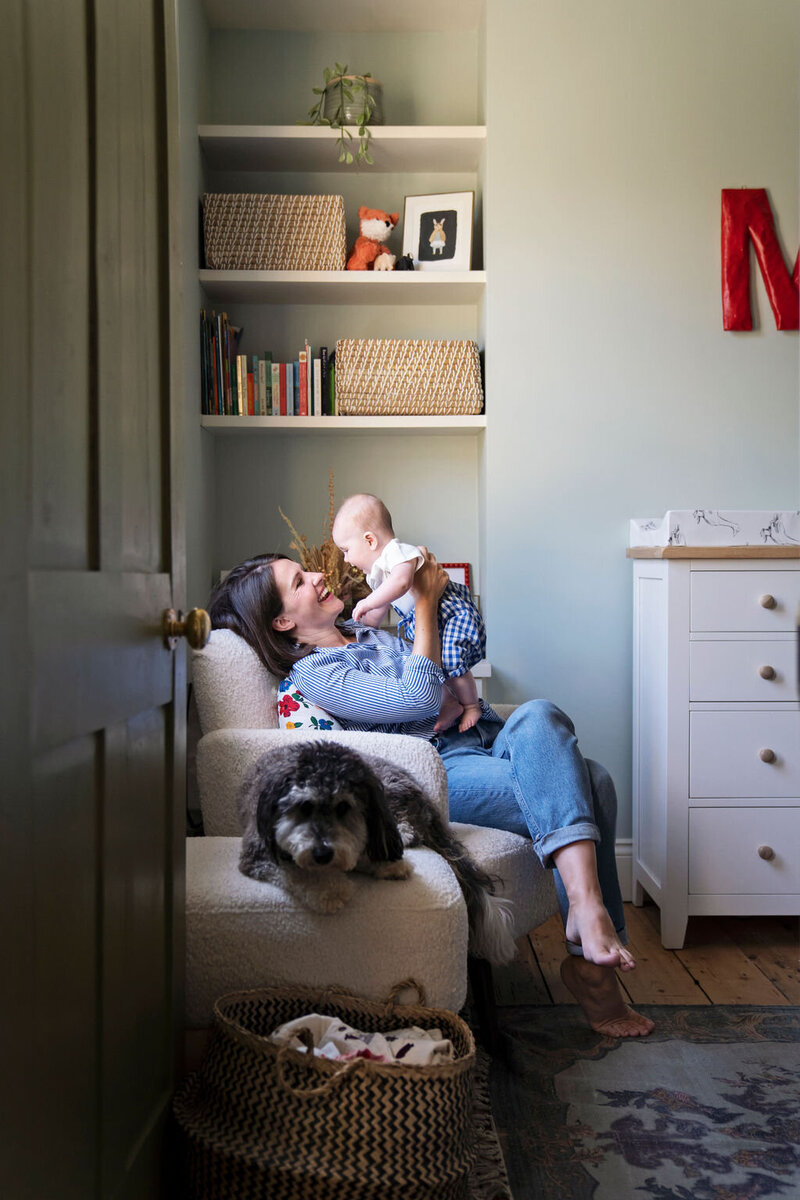 A mother lifts up her baby girl as she sits in her nursery with the family dog