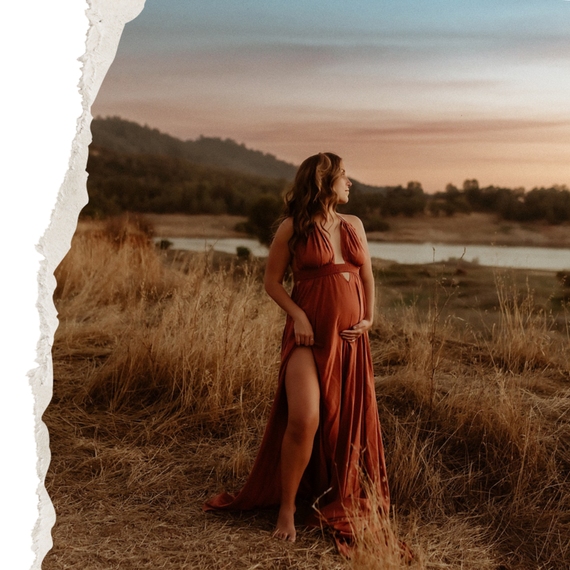 A pregnant woman in a red dress standing in a field at sunset.
