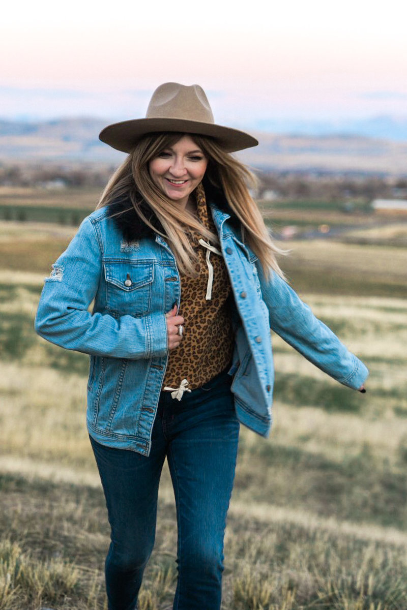 Stephanie with a jean jacket and hat on running through a field in Utah