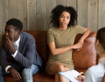 A couple appear to be arguing as they speak to a therapist with a clipboard. This could symbolize the hardships a relationship my encounter after an affair. Contact an online marriage counselor for support