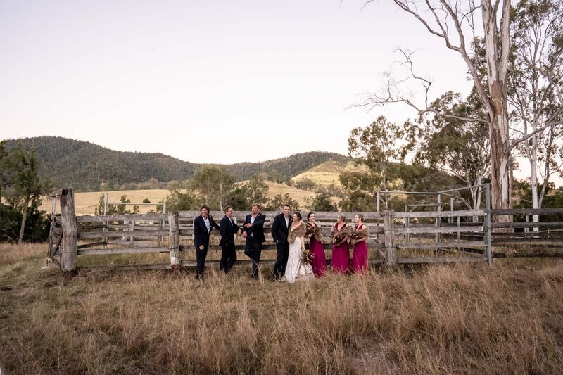 Wedding couple, Bridesmaids and Groom chatting and leaning on a farm fence