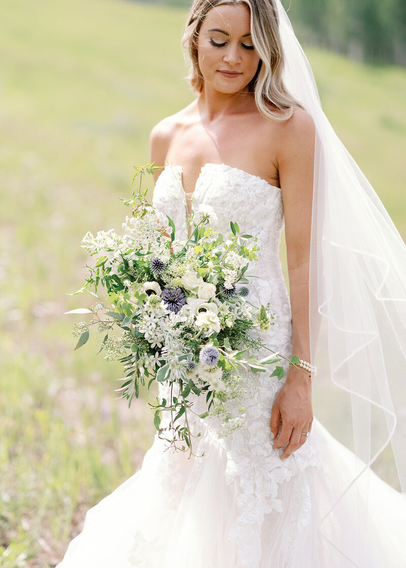 Testimonial photo, bride in flowing lace dress smiles at a camera with hills behind her