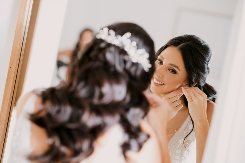 Bride putting her earrings in front of the mirror