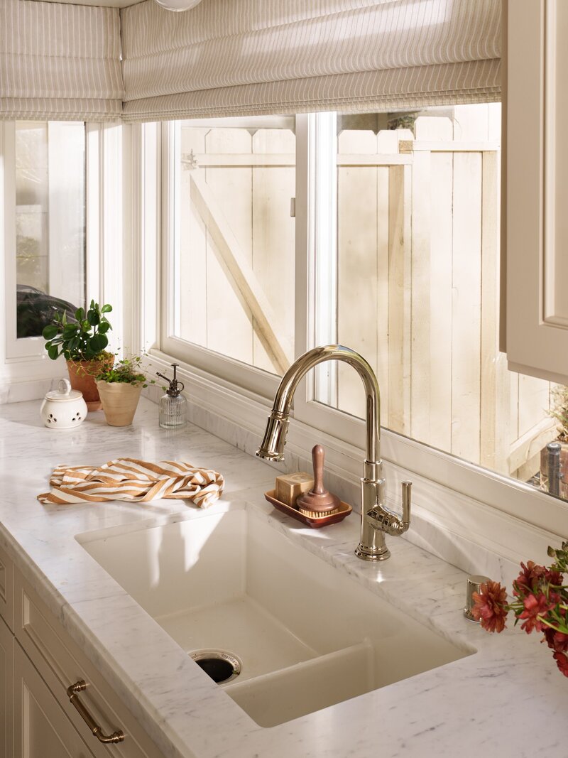 Kitchen remodel with woven pendant light above sink with custom window coverings, tan cabinetry, and marble countertops