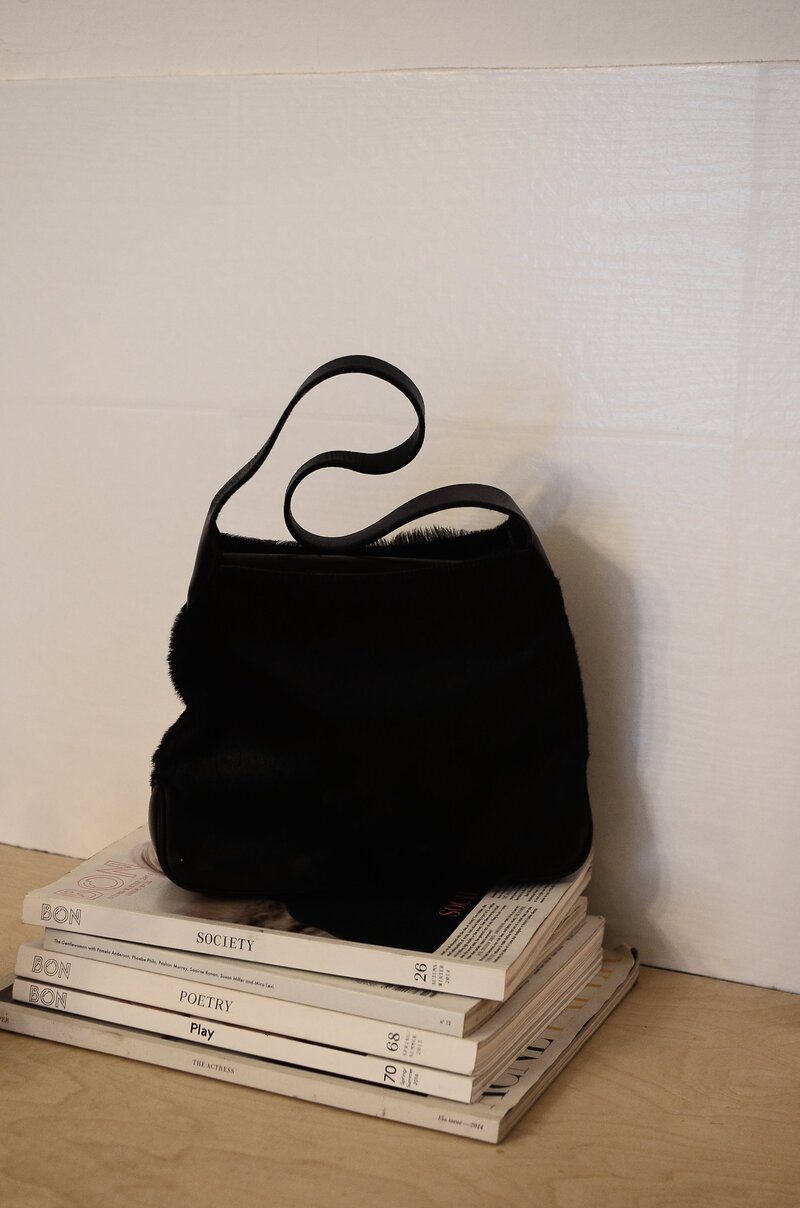 stack of fashion and design magazines with black handbag sitting on top