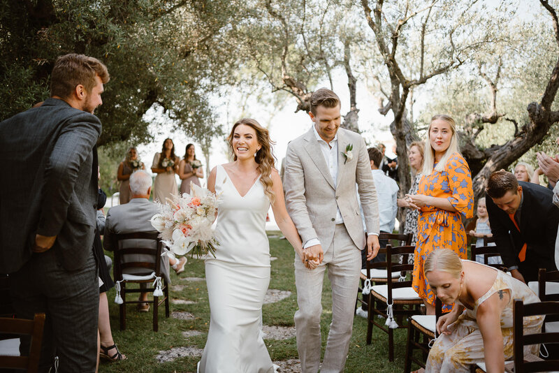 Bride and groom exit from the wedding ceremony under the olive trees at Villa Cicolina, in Tuscany