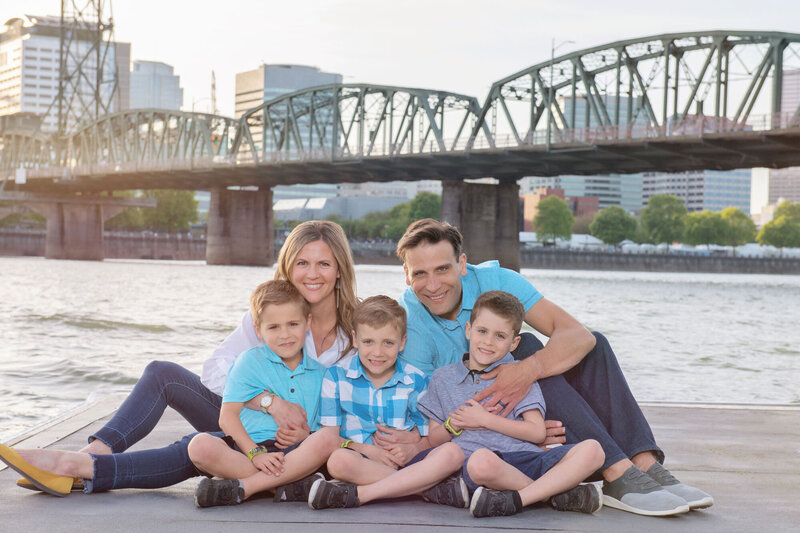 Picture of a family of five in front of a river with a bridge.