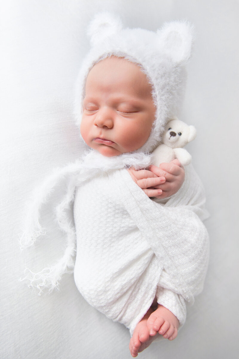 Sweet sleeping newborn baby with bear ear bonnet and teddy bear.