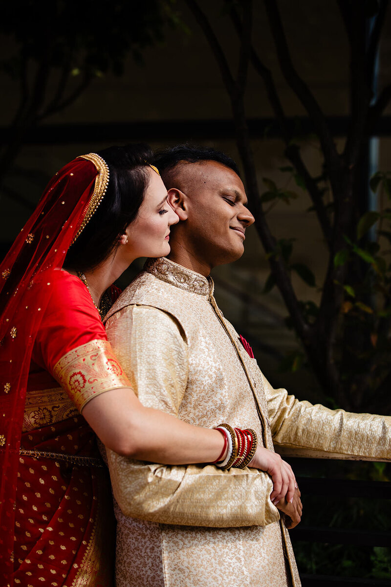 A bride and groom in traditional Indian wedding attire stand closely