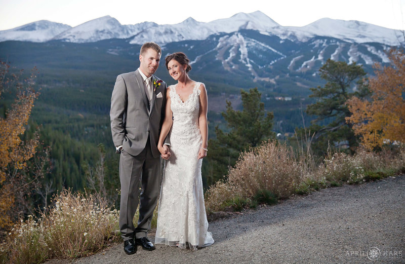 Couple just married holds hands at The Lodge at Breckenridge with the ski slopes off in the distance behind them