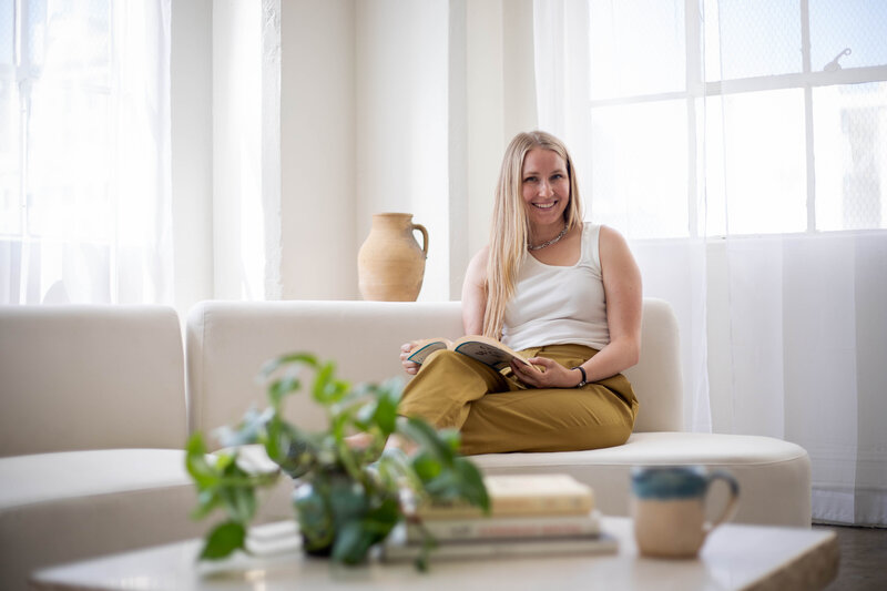 Krista Walsh, a website copywriter, on a white couch reading a book