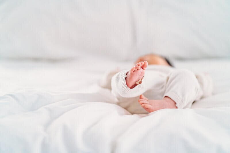 A softly focused image showing only the feet of a newborn baby against a white blanket, invoking a sense of peacefulness and purity.