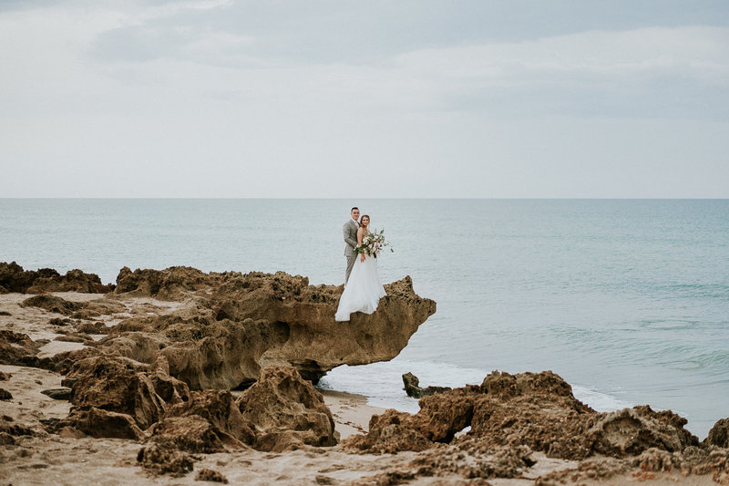 Eloping wedding couple stand on limestone rock formation over House of Refuge beach on Hutchinson Island Stuart FL