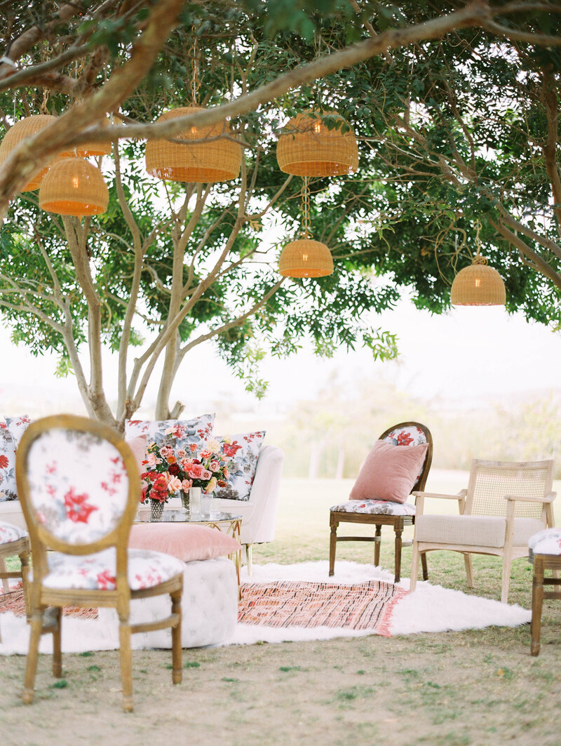 Outdoor wedding reception seating area with mismatched vintage chairs  under a tree with hanging straw chandeliers
