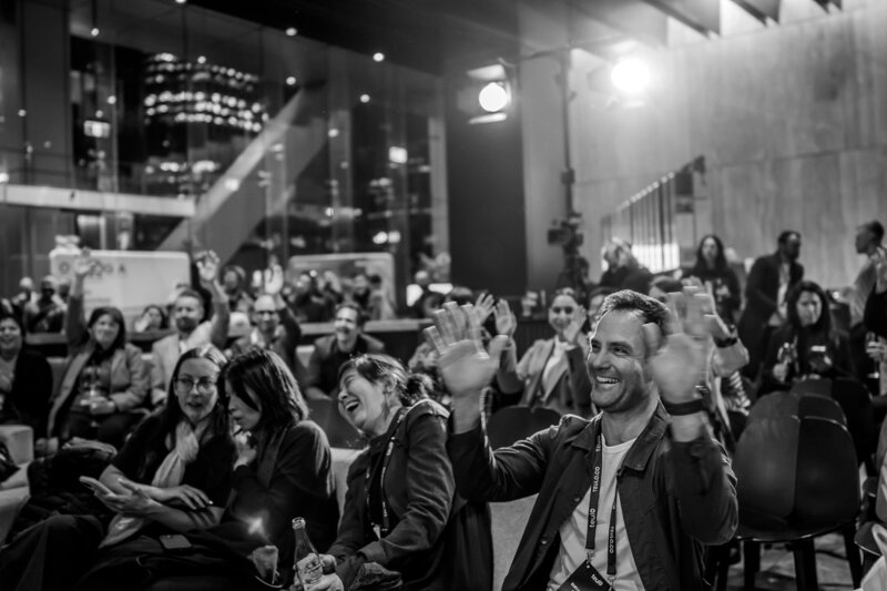 Black and white photo of people raising their hands and laughing at a architectural event in Auckland captured by Zanthe Vorsatz, Auckland Events Photographer