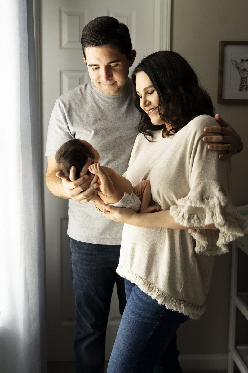 Mother and father smiling at baby in front of window by Atlanta newborn photographer