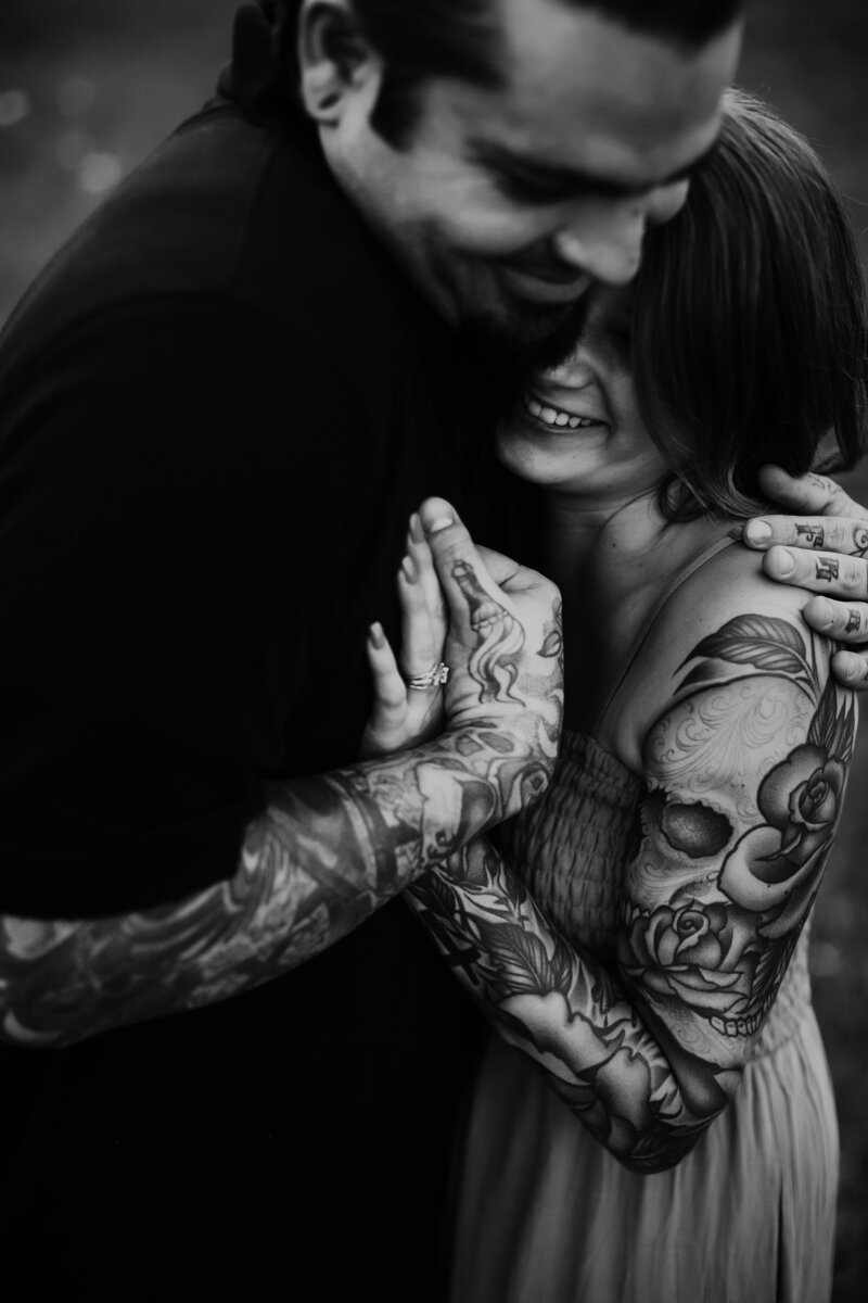 Black and white photo of tattooed couple hugging and holding hands