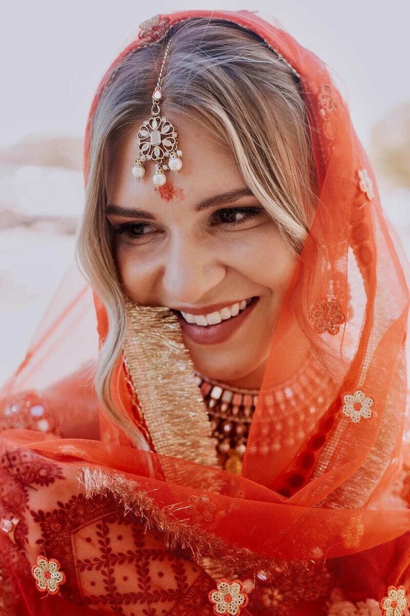 A bride wearing a bright red sari and beautiful makeup looks off in the distance