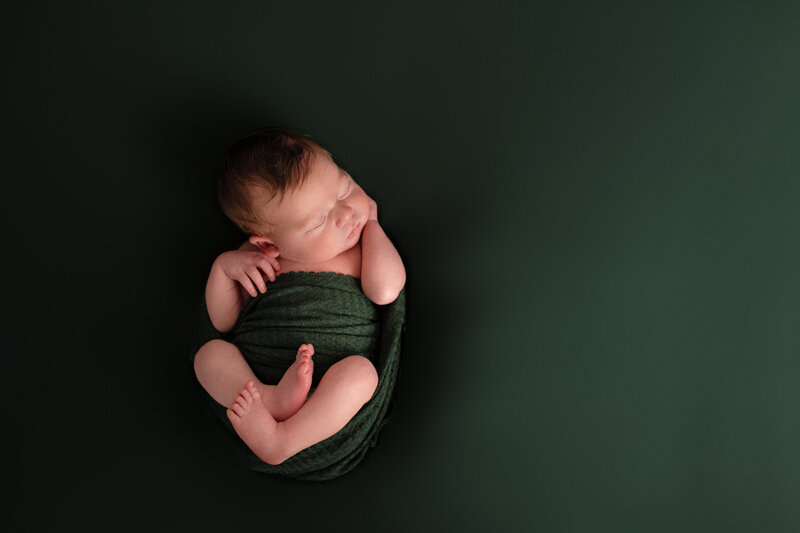 A newborn baby wrapped in a green blanket.