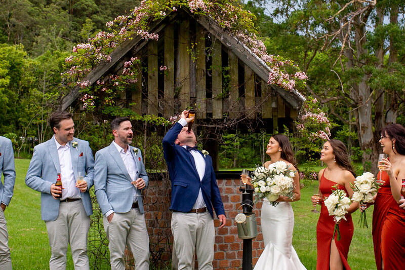 Groom drinks up a bottle of champagne with bridesmaids and groomsmen