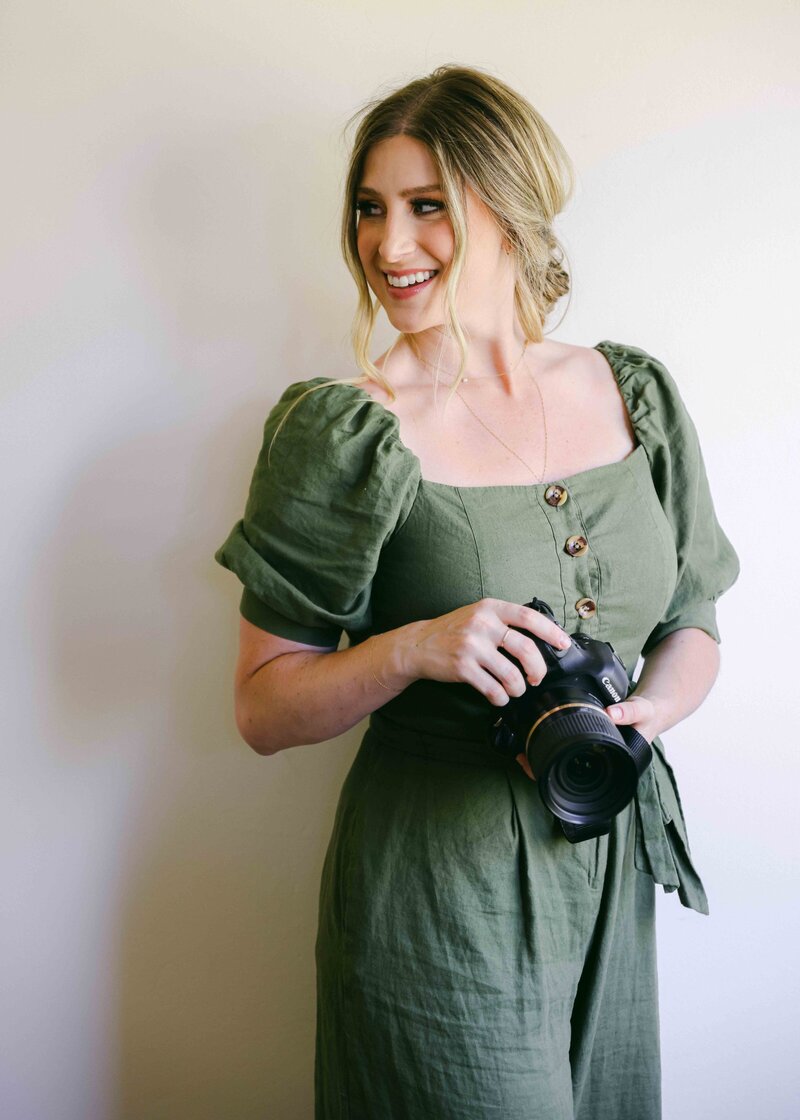 Chelsea Loren in a green jumpsuit by Gal Meets Glam holding a camera
