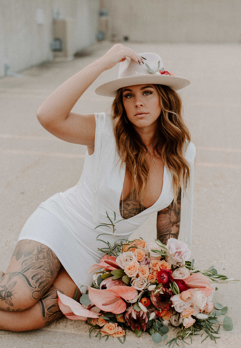 tattooed bride with bouquet holding her hat