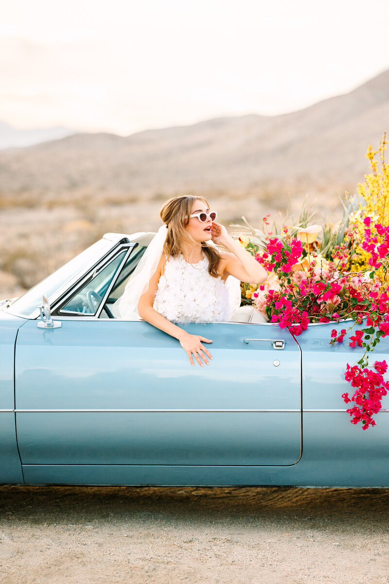 woman in vintage blue convertible car with florals and veil