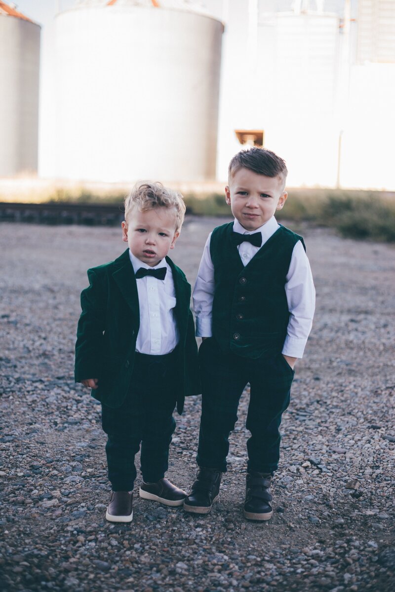 Two boys in green tuxedos posing for a photo in front of a silo, captured by Britt Elizabeth family photographer.