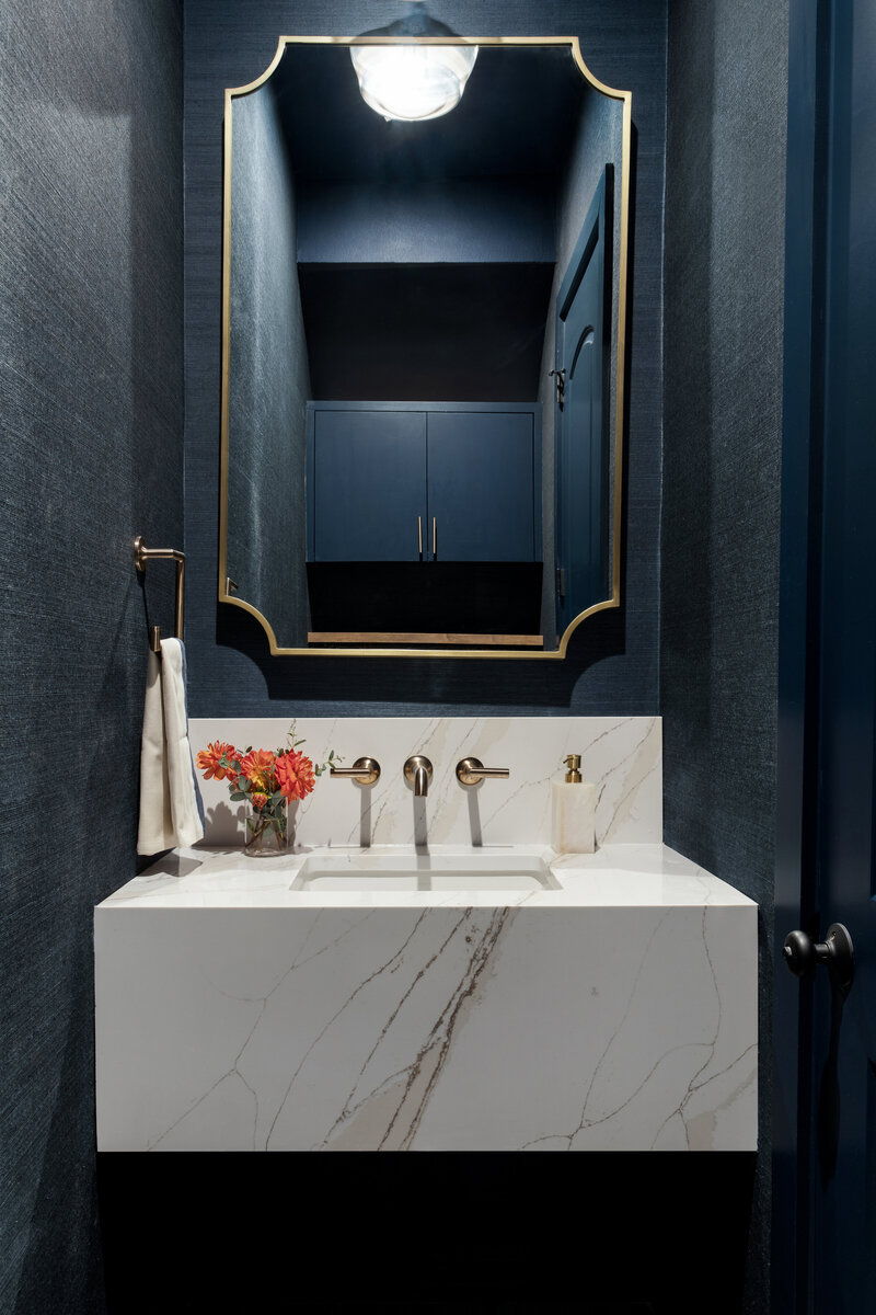 Powder bathroom vanity with dark blue, brass and marble accents. Floating pedestal sink.