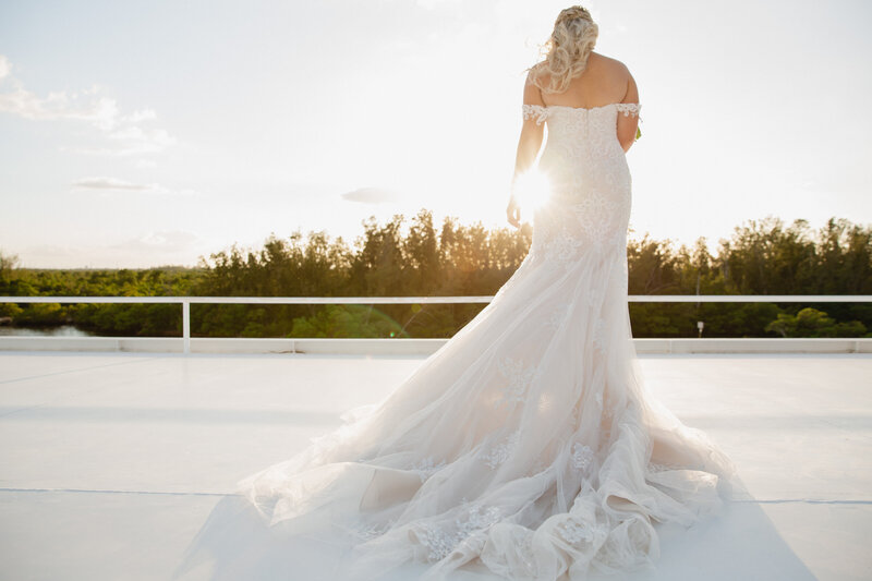View of a bride in wedding gown from behind as the sun shines through