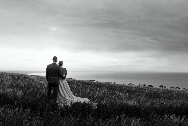 Bride and groom walking through a windswept field at Jack Rabbit Vineyard in Geelong, captured in timeless black and white.