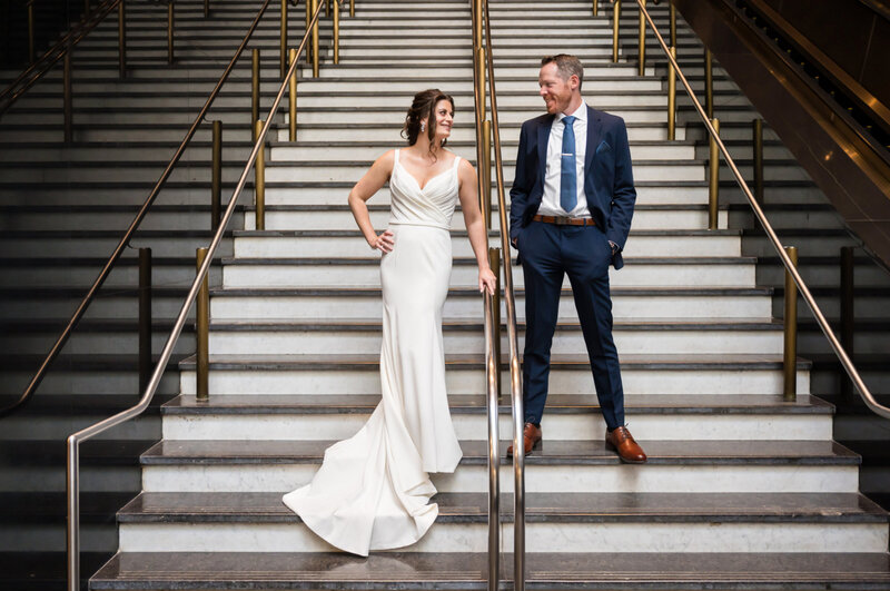 Bride and groom, standing on the grand staircase inside of Loews hotel in Philadelphia, PA