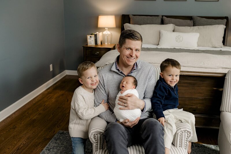 father holds newborn son with each of his older Sons sitting beside him in their Charlotte Area home  lifestyle newborn session