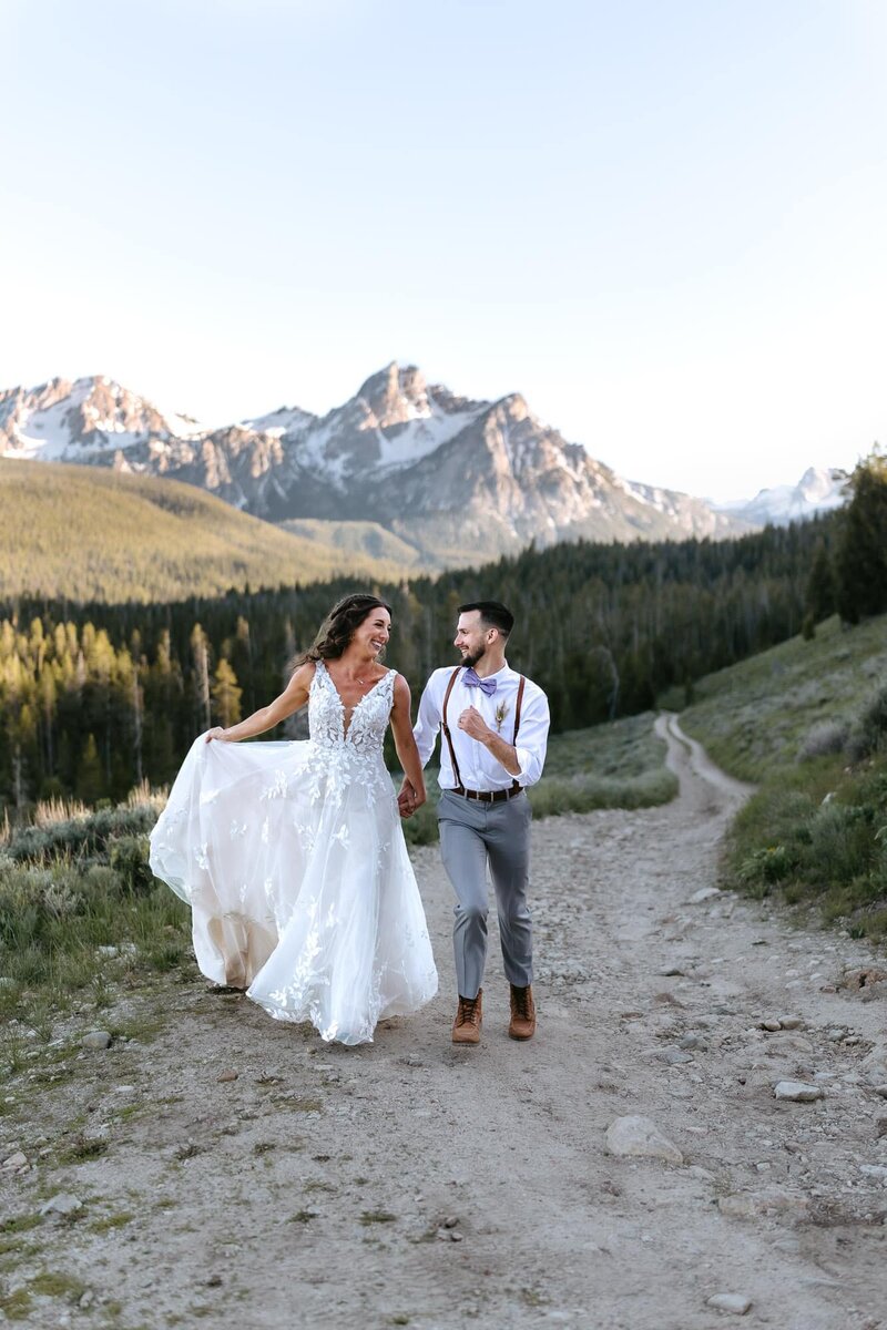 A couple holding hands on a dirt road in front of the Sawtooth mountains in Stanley, Idaho