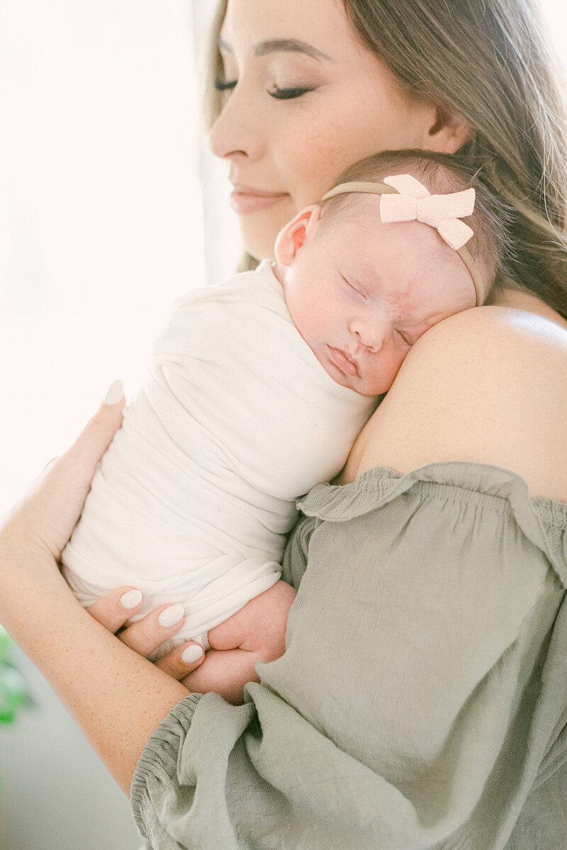 New mom with eyes closed holding sleeping newborn on shoulder and facing camera.