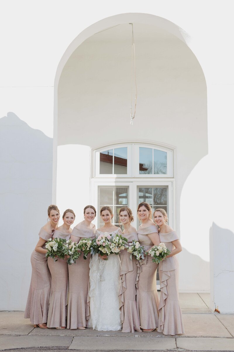 bride posed with bridesmaids in blush dresses