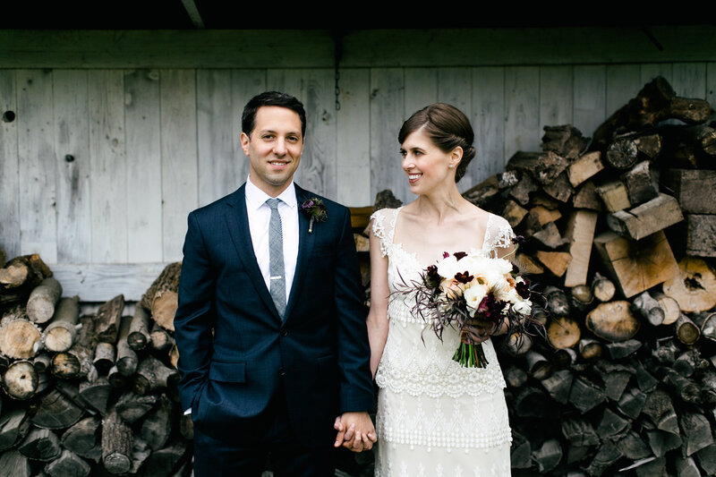 bride and groom in front of wood pile