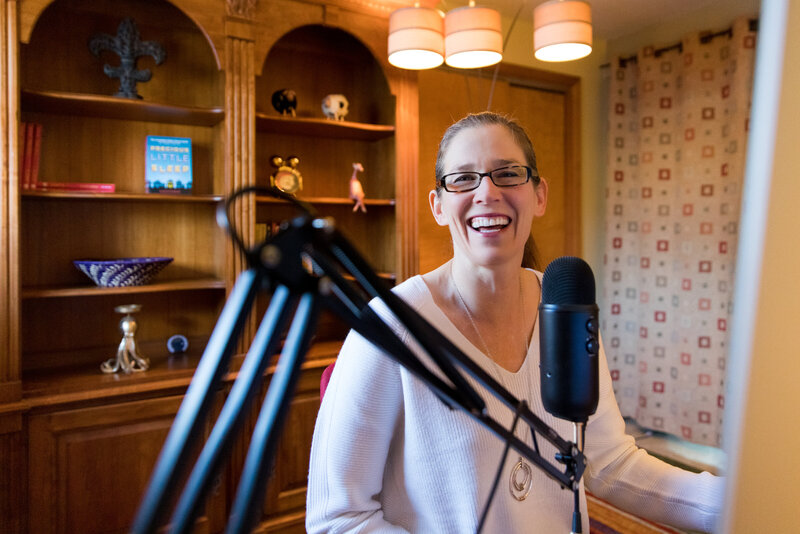 woman smiling while sitting behind a podcast microphone