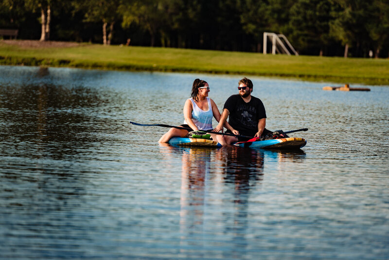 A man and a woman sit on paddle boards and laugh in the sunshine