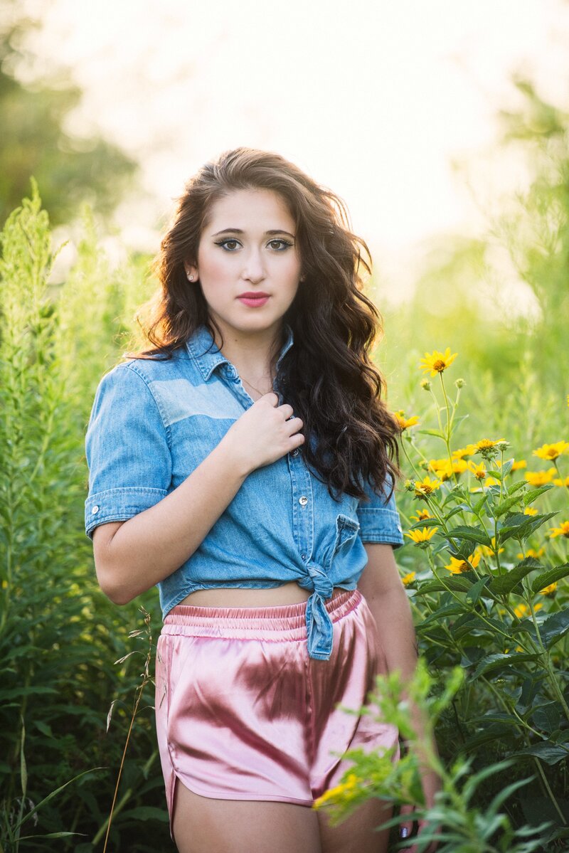 senior photo of girl in denim shirt and pink silk shorts in flowers