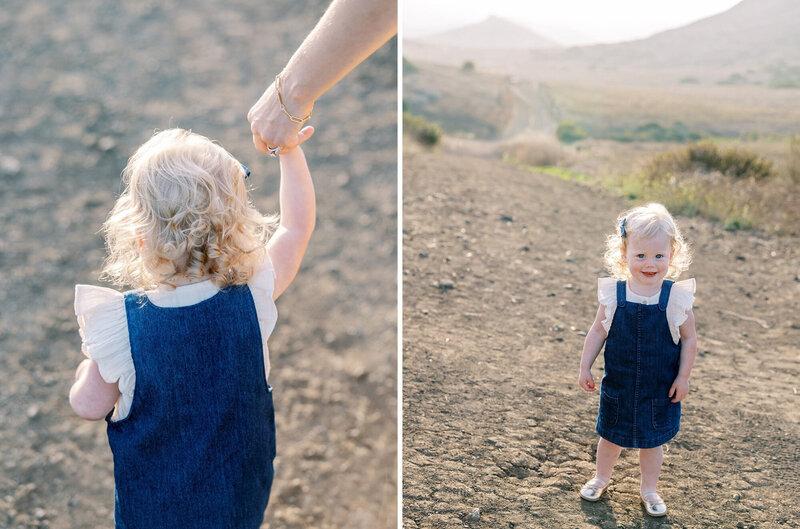 A little girl in a blue denim jumper holds her mom's hand during a child portrait session