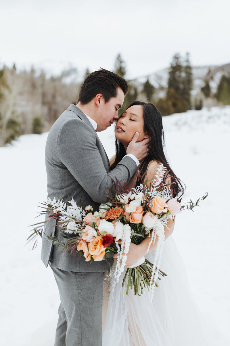 couple hugging in snow with wedding bouquet