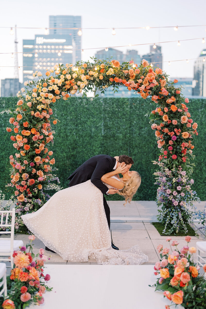 Bride and groom kissing at rainbow flower ceremony altar