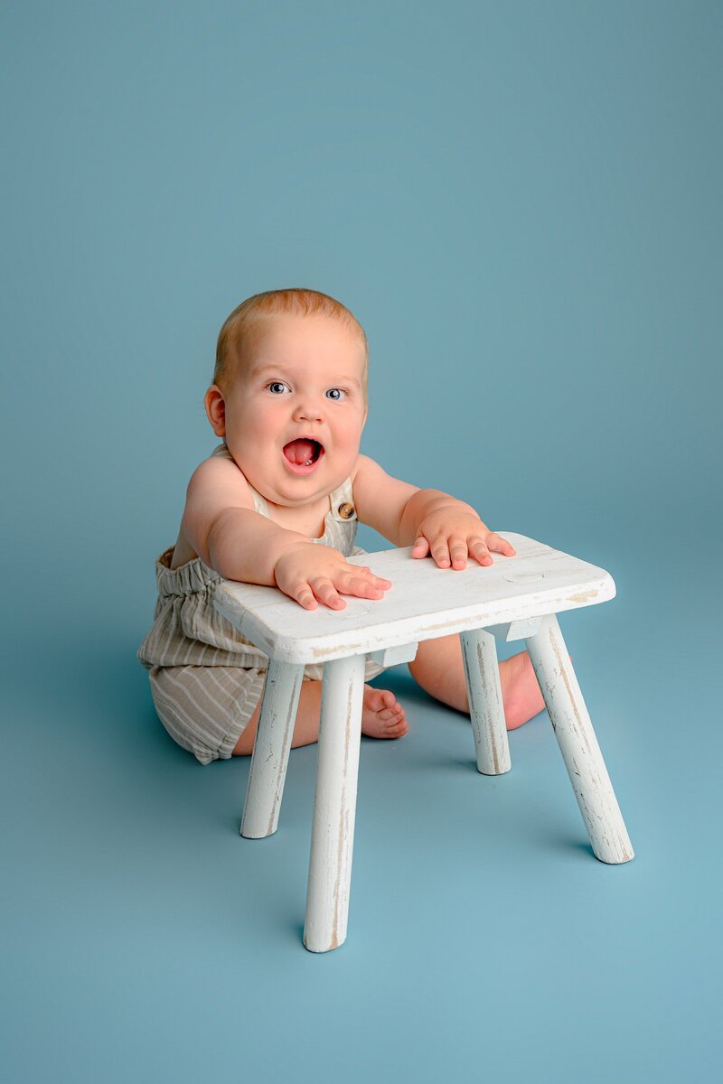 on blue background little boy sits holding onto bench
