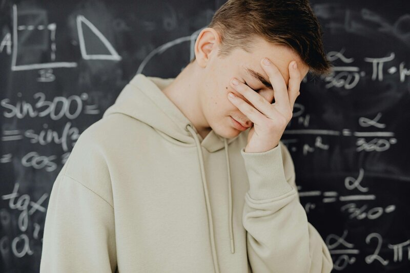 Student standing at blackboard with face covered