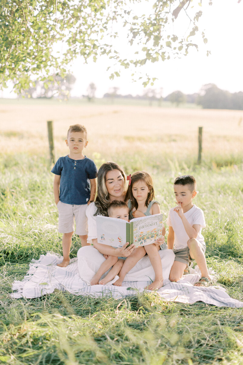 Mother reading a book to her kids on a blanket in a field