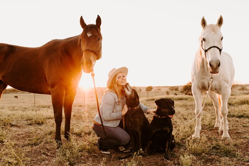 woman posing with dogs and horses